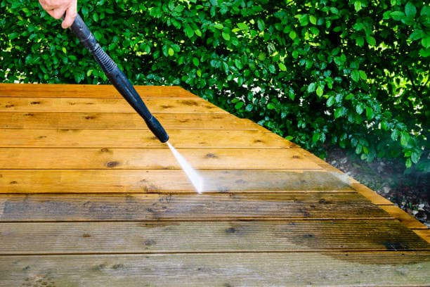 A wooden area being powerwashed, halfway clean.